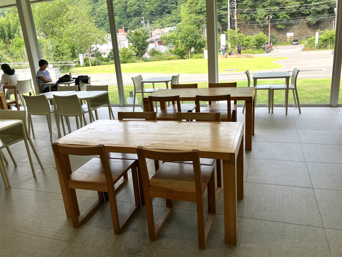 大きなガラス窓から芝生と山が見える木のテーブル席