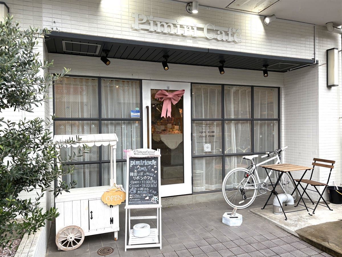 pimiri cafeの外観。白いタイルの壁とピンクの大きなリボンのドア