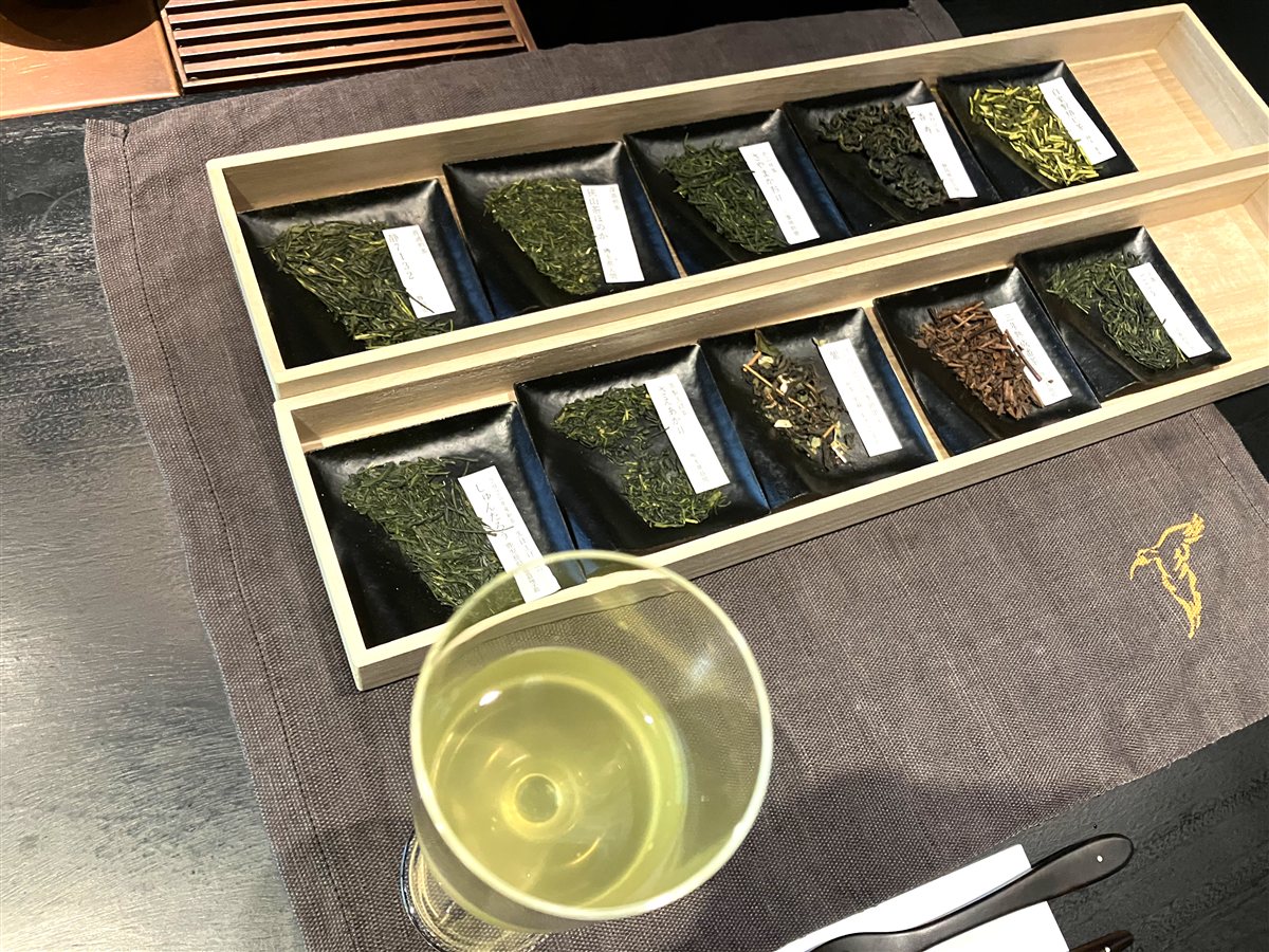 木箱に並んだ約10種類の茶葉と冷茶のグラス