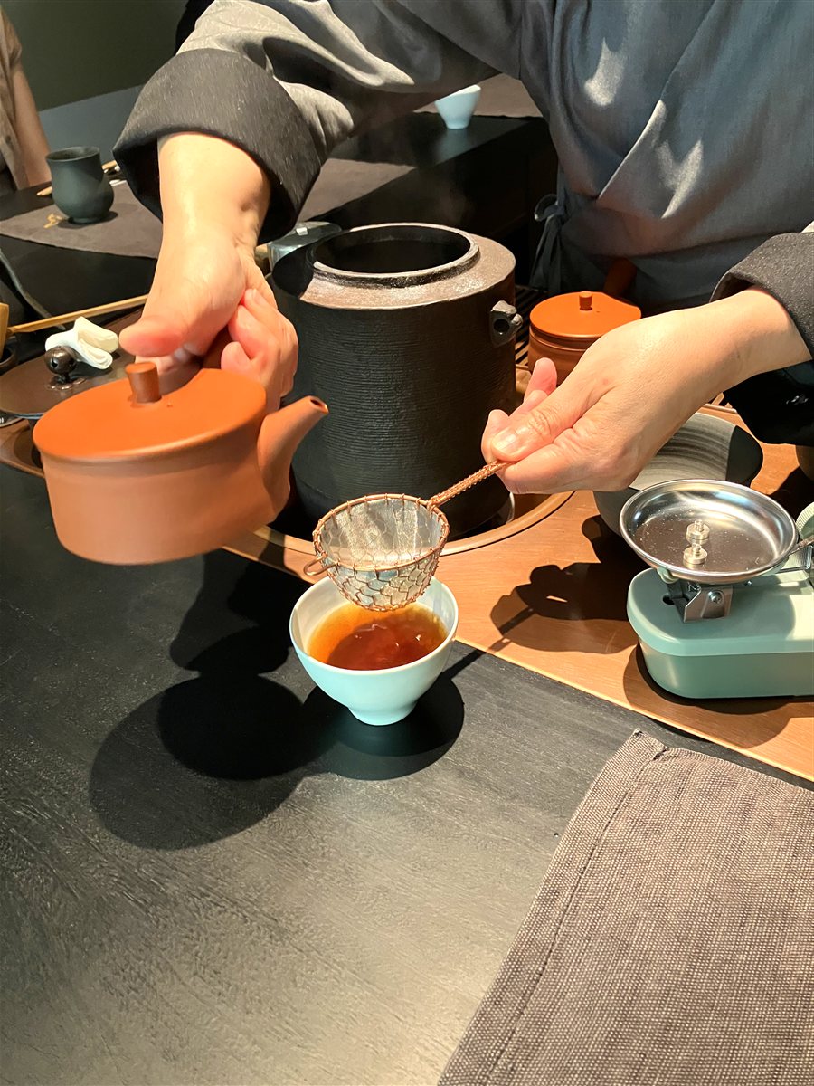 茶師が朱色の急須から茶こしを通してほうじ茶を注ぐ様子